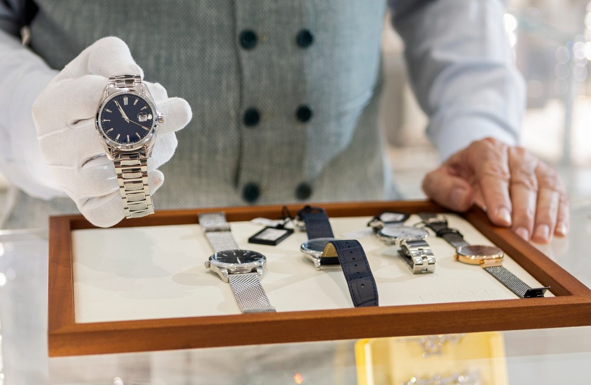 Image of an elderly man with a white glove holding a watch over a tray of watches.